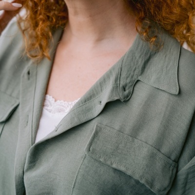 Blusa verde-acinzentada com bolso e botões e pendente dourado, cabelo ruivo encaracolado