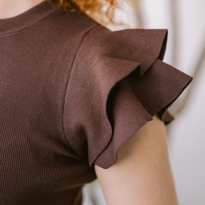 T-shirt castanha de malha com folhos nas mangas, vista de perto no ombro de uma pessoa com cabelo ruivo.