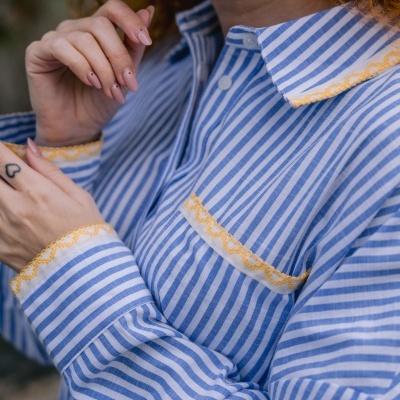 Camisa riscada azul e branca com bordado amarelo nas mangas, colarinho e bolso.