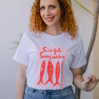 T-shirt branca com desenho de peixes vermelhos e texto em inglês, combinada com jeans azuis, com planta no fundo.