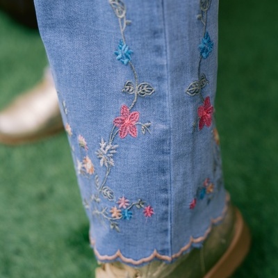 Calças de ganga azul com bordados florais e botas douradas