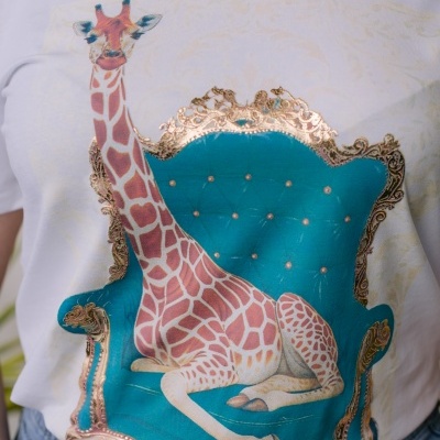 T-shirt branca com estampa de girafa sentada num sofá azul com moldura dourada