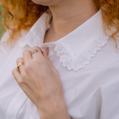 Camisa branca com gola de renda e mão com anel e tatuagem