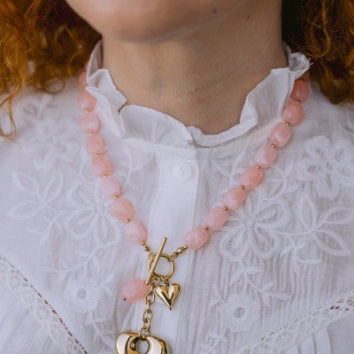 Colar com contas cor-de-rosa e pendentes dourados em forma de coração, usado com blusa branca bordada.