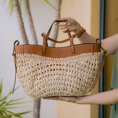 Saco de mão em material trançado bege com parte superior em pele castanha segurado por mãos femininas