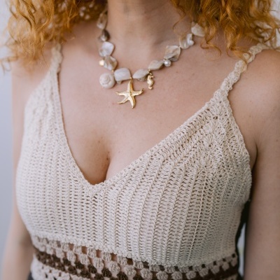 Colar feminino com pendentes dourados de estrela-do-mar, usado com top bege e saia preta.