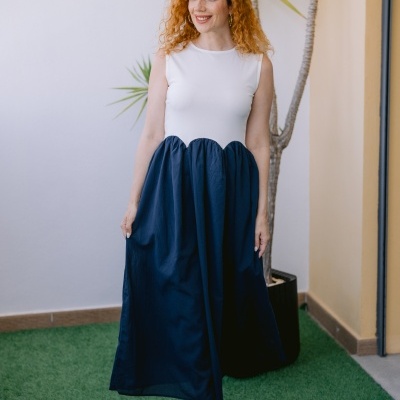 Mulher com vestido branco e azul escuro em ambiente exterior com planta.