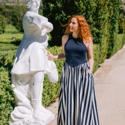 Mulher com vestido comprido azul e branco ao lado de estátua branca no jardim