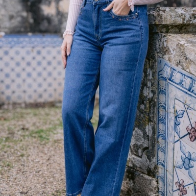 Calças de ganga azuis com corte largo e camisola rosa junto a muro com azulejos