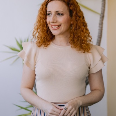 Mulher ruiva com blusa bege de mangas curtas e saia riscada