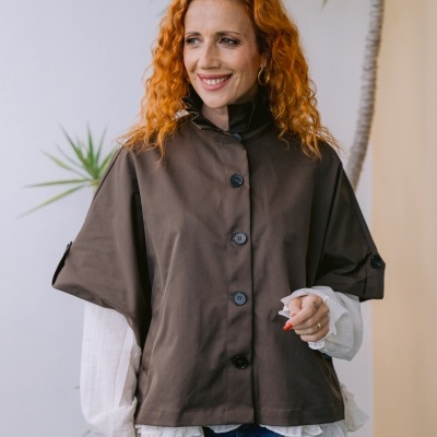 Mulher com casaco castanho, camisa branca e calças de ganga junto a planta