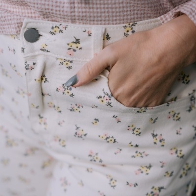 Calças florais brancas com mão no bolso e camisa rosa de padrão vichy