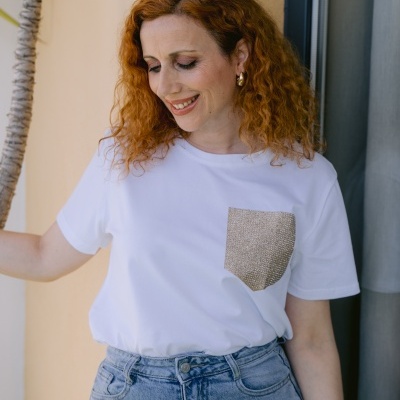 Mulher com blusa branca com bolso bege e calças de ganga azul claro encostada na parede