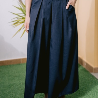 Culottes azuis escuros com pregas e bolsos, usadas por mulher com botas castanhas.