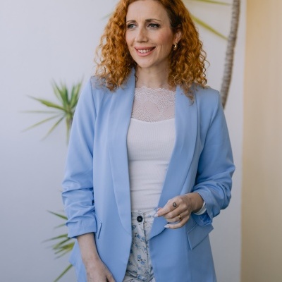 Mulher com blazer azul claro e calças florais junto a planta