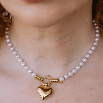 Colar de pérolas brancas com pendente de coração dourado no pescoço de mulher