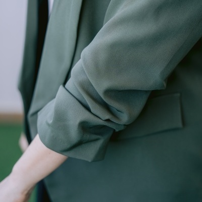 Blazer verde com manga dobrada e bolso à vista junto ao braço de uma pessoa.