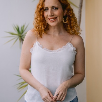 Mulher vestindo blusa branca com alças e calças de ganga, com plantas ao fundo