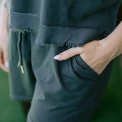 Peça de vestuário verde escuro com bainha desfiada e mão feminina no bolso