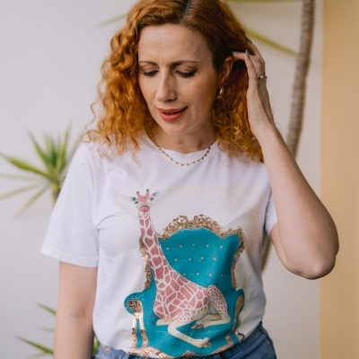 Mulher com t-shirt branca com estampa de girafa numa cadeira azul e calças de ganga