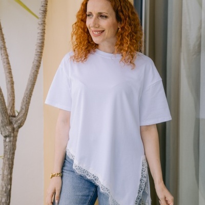 Mulher de cabelo ruivo com camisola branca de manga curta e jeans azuis claros em ambiente exterior.