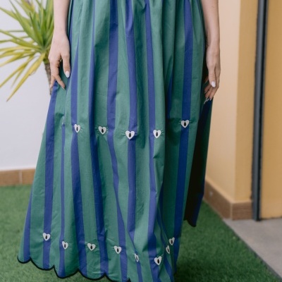 Saia comprida listrada verde e azul com corações brancos, usada com botins dourados, numa área exterior com relva