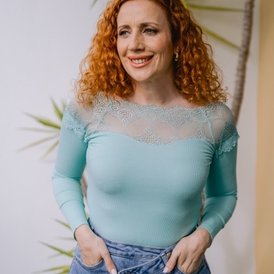 Mulher ruiva com camisola azul claro e calças de ganga em ambiente com planta verde