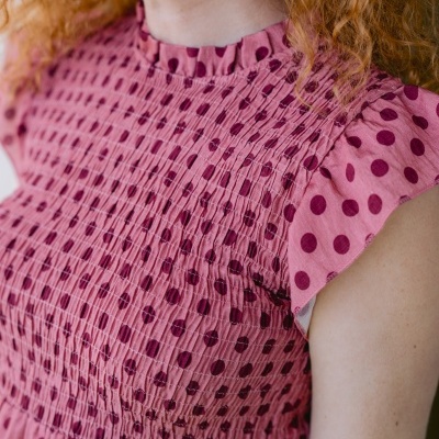 Blusa rosa com bolinhas roxas e detalhes franzidos perto do pescoço.