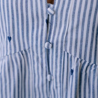 Peça de roupa com riscas verticais azuis e brancas e pequenos corações azuis bordados