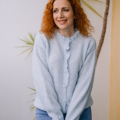 Mulher com camisola azul clara e cabelo ruivo encaracolado junto a planta