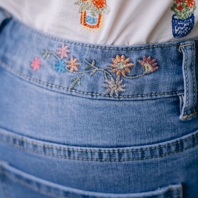 Calças de ganga azuis com bordados florais e parte superior branca bordada