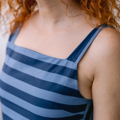 Vestido azul às riscas mostrado em mulher ruiva próximo do rosto e ombro.
