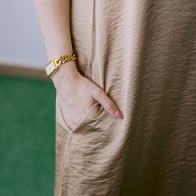 Braço de mulher com relógio dourado e vestido bege com bolso