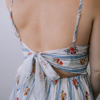 Vestido branco com riscas azuis e flores coloridas, laço grande nas costas da mulher.
