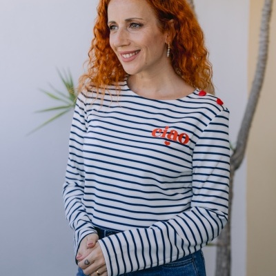 Mulher com camisola riscada branca e azul com texto ciao e calças de ganga azuis