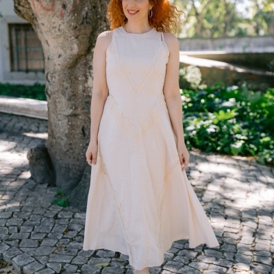 Mulher com vestido creme e sapatos dourados em calçada de pedra junto a árvore