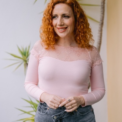 Mulher com blusa rosa de renda e jeans cinzentos com plantas ao fundo