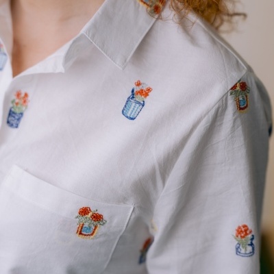 Camisa branca com bordados de vasos de flores coloridos.