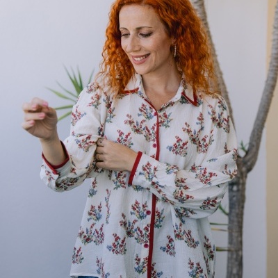 Camisa branca de tecido leve com padrão floral e detalhes vermelhos usada por mulher com calças de ganga