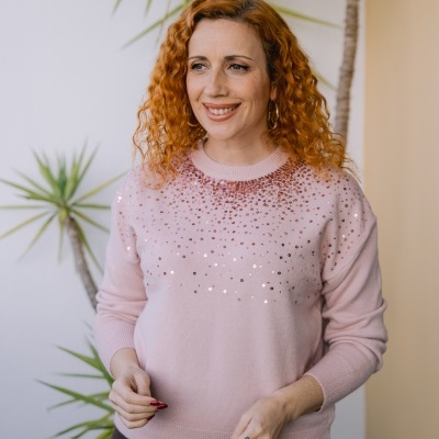 Mulher com camisola rosa clara com lantejoulas e saia preta junto a plantas verdes