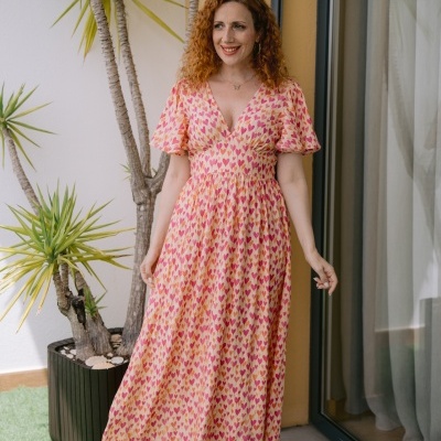 Vestido comprido com padrão de corações usados por mulher junto a plantas e porta de vidro.