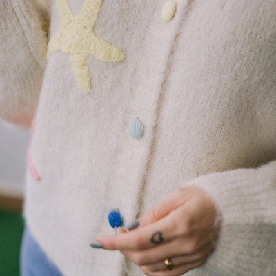 Cardigan de malha creme com botões coloridos e estrela-do-mar amarela em relevo