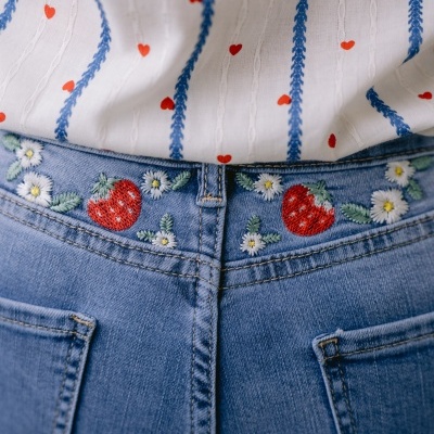 Calças de ganga com bordados de morangos, flores e uma camisola branca com riscas azuis e corações vermelhos.