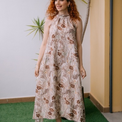 Vestido comprido floral bege com sandálias trançadas castanhas num ambiente exterior com relva e plantas.