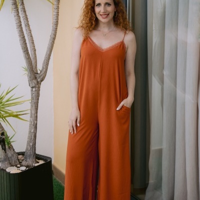 Mulher de macacão laranja com alças finas num ambiente de varanda com plantas.