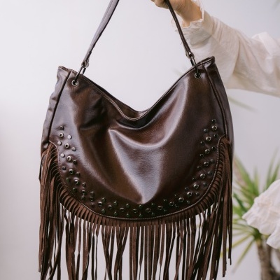 Mala castanha em pele com franjas e tachas decorativas segurada à mão