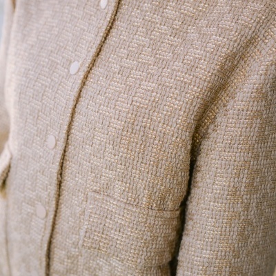 Casaco bege em tweed com botões brancos e detalhes dourados.