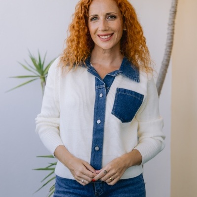 Camisola branca com detalhes em ganga azul e calças de ganga azuis vista até à cintura, mulher com cabelo ruivo encaracolado.