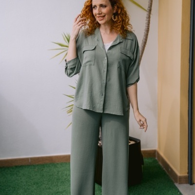Conjunto feminino verde água e sapatos dourados com planta e relva artificial ao fundo
