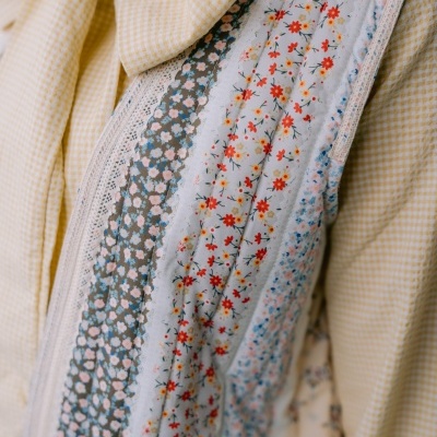 Peça de vestuário amarela com padrão xadrez e detalhes florais com rendas.